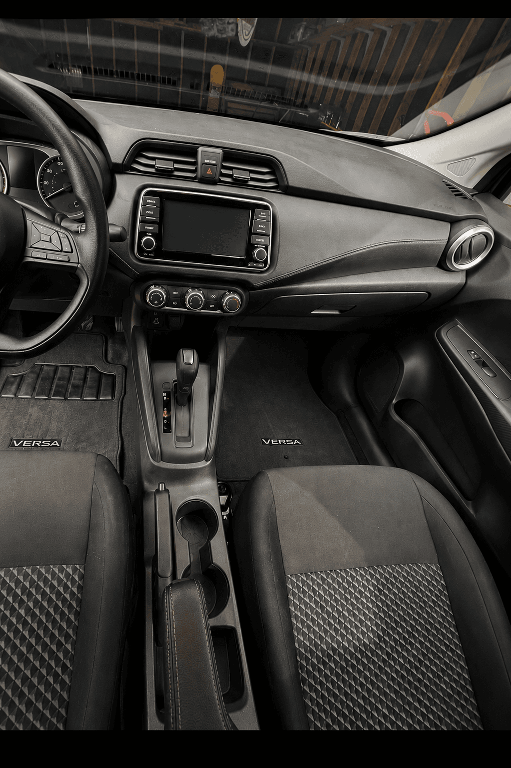 Nissan Versa interior featuring a black dashboard, touchscreen, gear shifter, and patterned fabric seats.
